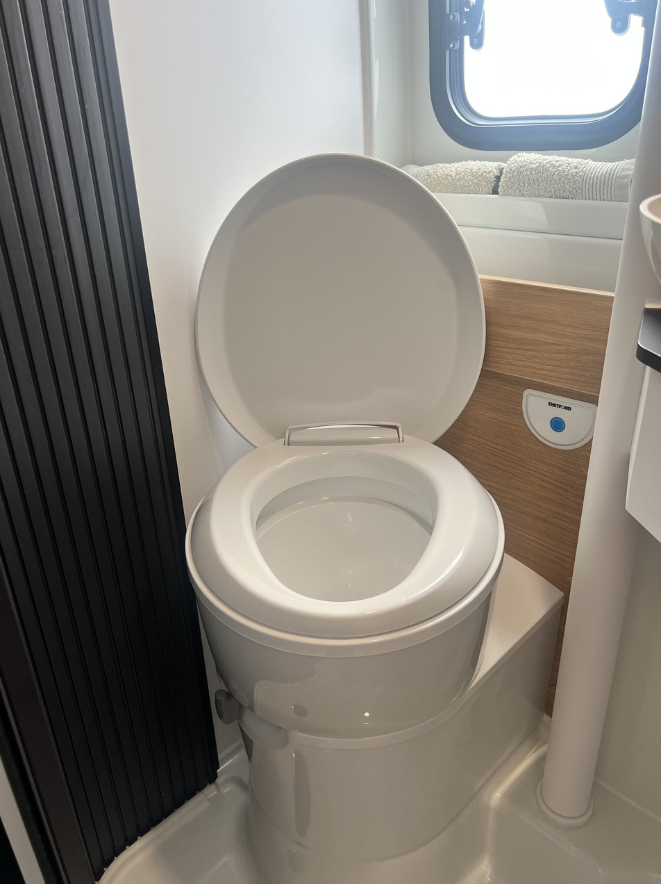 Baño pivotante con inodoro del Adria Twin 640 SGX | Activans Primer plano del inodoro cassette abierto en el baño pivotante amplio del Adria Twin 640 SGX – camper en alquiler Cataluña