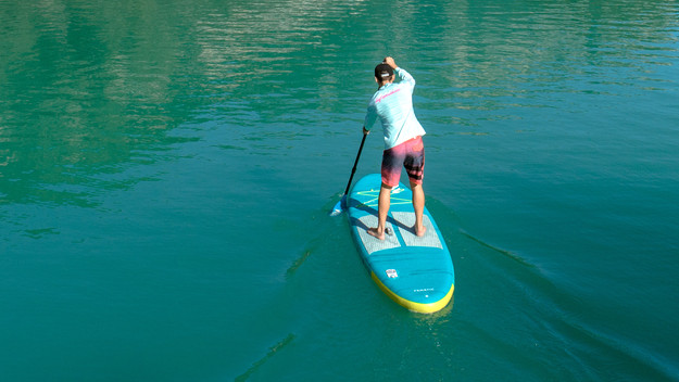 On voit une personne pratiquant le paddle par derrière, pagayant sur des eaux calmes.