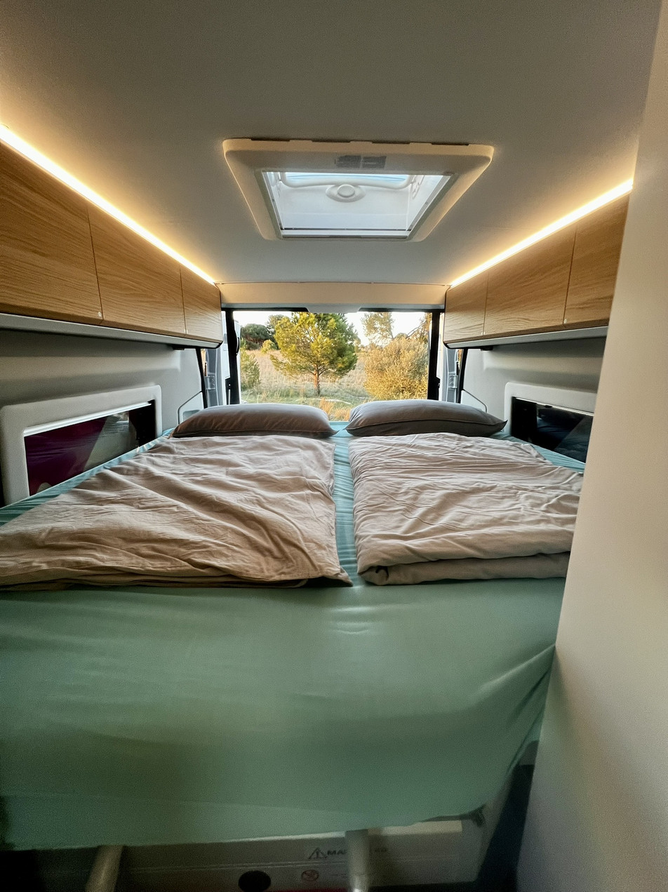 Alquiler camper España – cama trasera doble 185x190 | Adria Twin 640 SGX | Activans Cama trasera doble con sistema manual de regulación en altura, hecha con ropa de cama y puertas traseras abiertas a la naturaleza en Adria Twin 640 SGX