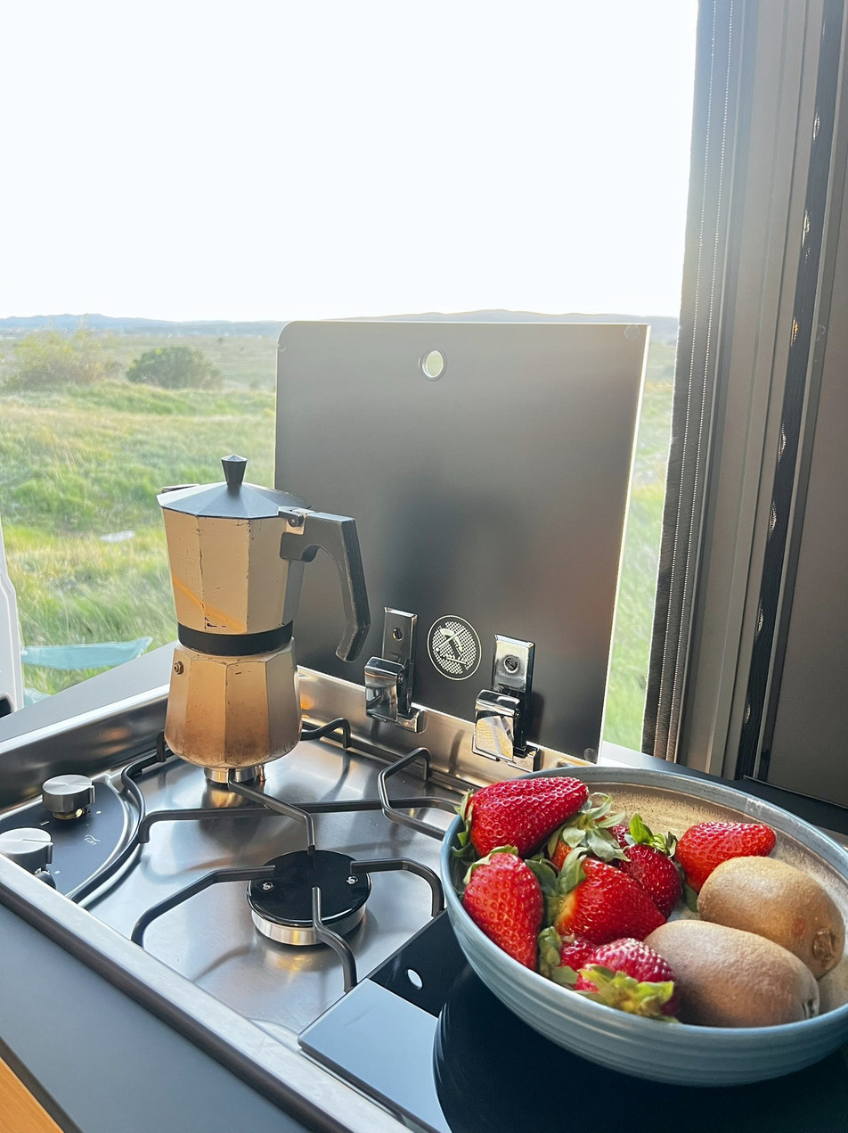 Alquiler camper Costa Brava España – cocina con cafetera italiana | Adria Twin 640 SGX | Activans Cocina de gas con cafetera italiana en camper, puerta abierta con vistas a la naturaleza en Adria Twin 640 SGX